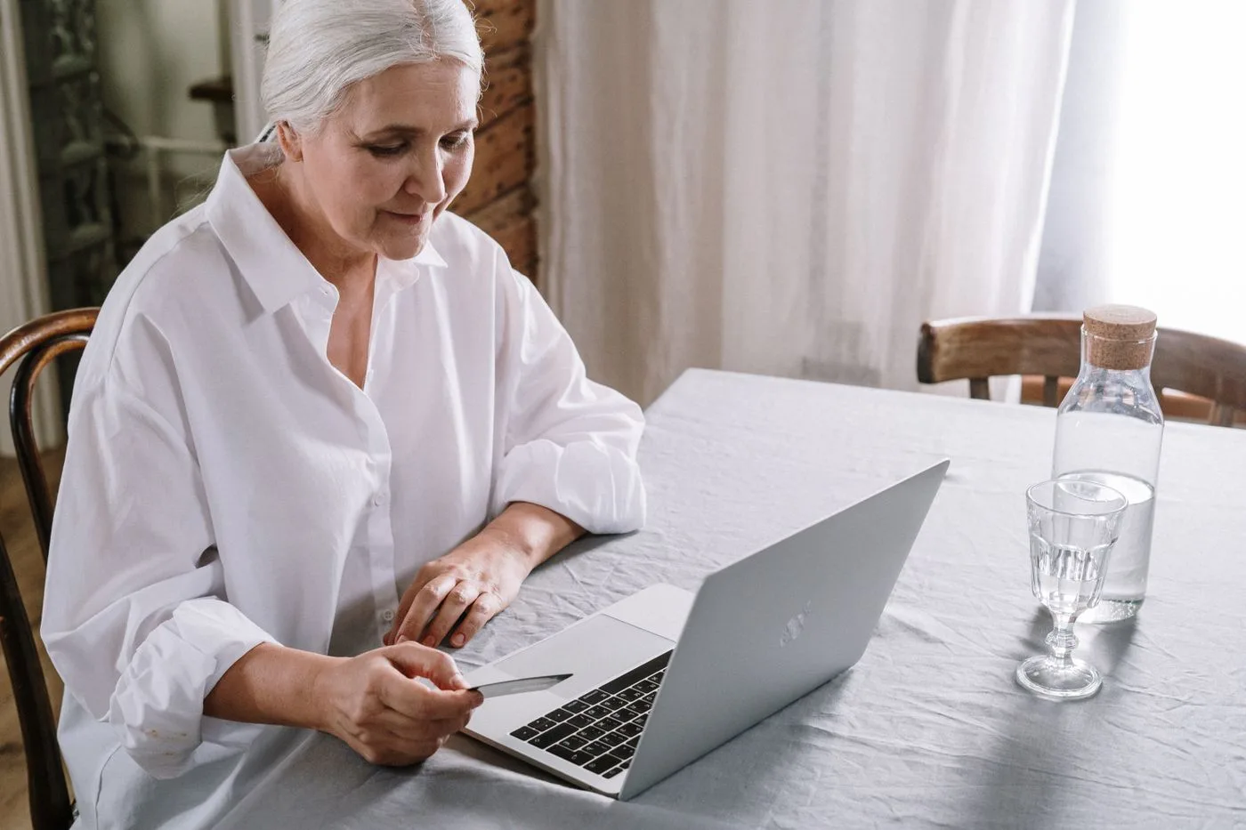 An older woman smiling while writing her dating profile on a laptop at home